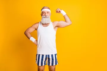 Tafelkleed Foto van een vrolijke positieve aantrekkelijke knappe oude man die zijn spieren demonstreert en je aandachtig aankijkt met de hand op de taille geïsoleerde levendige kleur gele achtergrond © deagreez