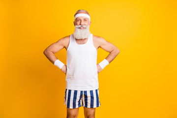 Photo of cheerful positive old man smiling toothily holding hands on waist demonstrating muscles...