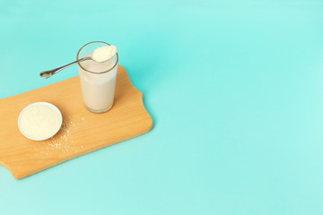 Collagen powder and yogurt in a glass with a spoonful on top on blue background.