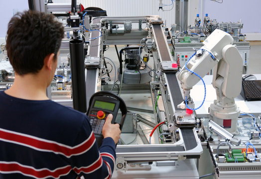 Man is programming robotic arm with teach panel  which is integrated on smart factory production line. industry 4.0 automation line which is equipped with sensors and robotic arm. Selective Focus.