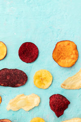 Dried fruit and vegetable crisps, shot from above with copy space. Healthy vegan snack, an organic food flat lay pattern on a blue texture