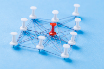 network with red and white pins and string, An arrangement of colorful pins linked together with string on a blue background suggesting a network of connections.