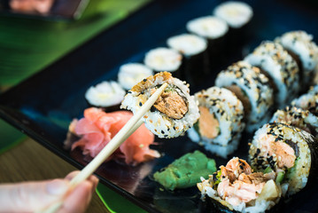 Eating roll sushi in japanese restaurant, hand with chopsticks closeup.. California Sushi roll set with salmon, vegetables.