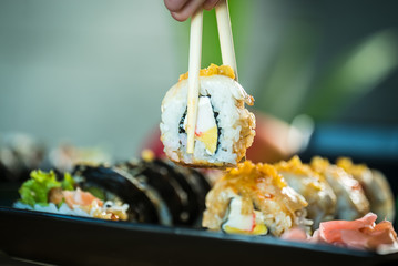 Eating roll sushi in japanese restaurant, hand with chopsticks closeup.. California Sushi roll set...