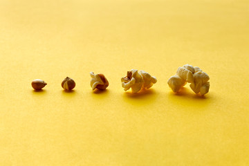 Fototapeta na wymiar Closeup of different stages of microwave popcorn preparation on a yellow background with copy space. From corn to popcorn in a horizontal row.