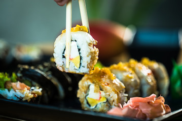 Eating roll sushi in japanese restaurant, hand with chopsticks closeup.. California Sushi roll set with salmon, vegetables.