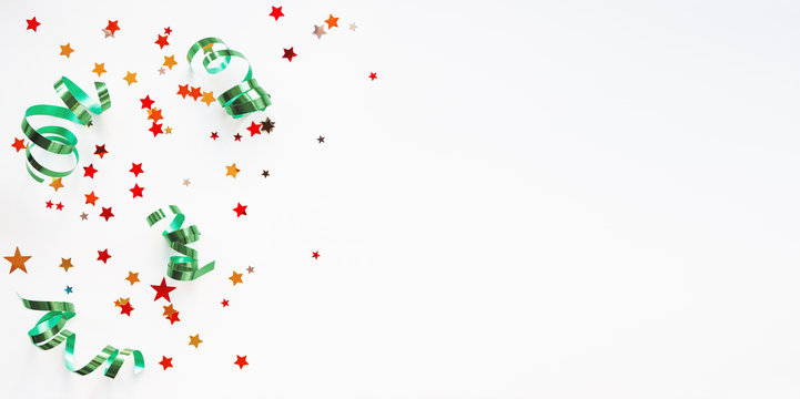 Holiday Background With Colorful Red Stars Confetti And Green Curly Ribbon. Christmas And New Year Decorations.