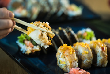 Eating roll sushi in japanese restaurant, hand with chopsticks closeup.. California Sushi roll set with salmon, vegetables.