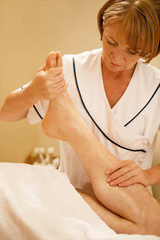 Obraz na płótnie Canvas Female massage therapist massaging man's leg at spa center.