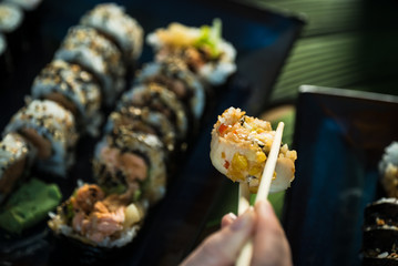 Eating roll sushi in japanese restaurant, hand with chopsticks closeup.. California Sushi roll set with salmon, vegetables.