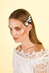 Medium close-up shot of a young stylish European girl with a cambered hair clip in her long straight hair. The hairpin is made of white glazy material in the form of a bow-knot with a black stripe.  © RedUmbrella&Donkey