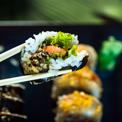 Eating roll sushi in japanese restaurant, hand with chopsticks closeup.. California Sushi roll set with salmon, vegetables.
