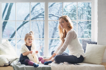 Mother and daughter in the living room sits on the window sill in winter morning