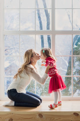 Fototapeta na wymiar Mother and daughter in the living room sits on the window sill in winter morning