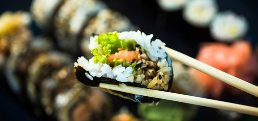 Eating roll sushi in japanese restaurant, hand with chopsticks closeup.. California Sushi roll set with salmon, vegetables.