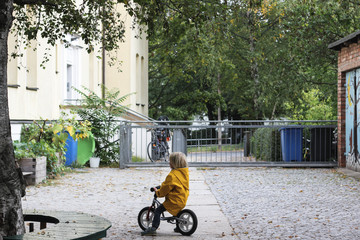 A child boy in a yellow jacket on a little bicycle at the yard outside