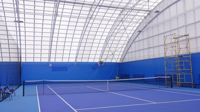 Tilt down shot of empty indoor tennis court with globe shaped roof, blue carpet and net