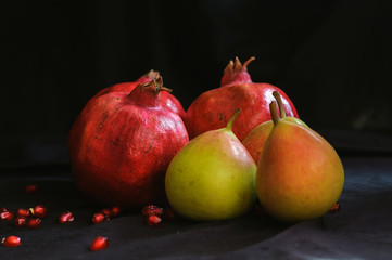 pomegranates and pears on a dark background and with scattered pomegranate seeds