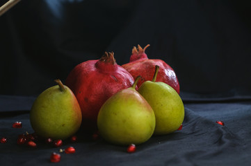 pomegranates and pears on a dark background and with scattered pomegranate seeds