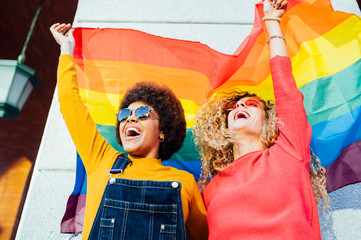 Two women friends hanging out in the city waving LGBT with pride flag