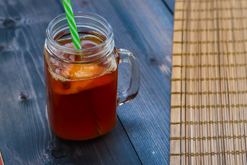 On a dark wooden tabletop, a glass mug of tea with lemon and a straw.