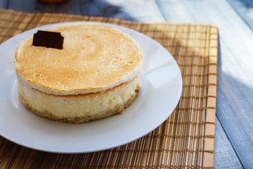 On a light tabletop on a straw napkin on a white dish, a classic cheesecake