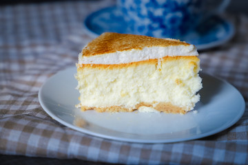 Close-up of a piece of classic cheesecake cake on a white dish and a checkered linen napkin