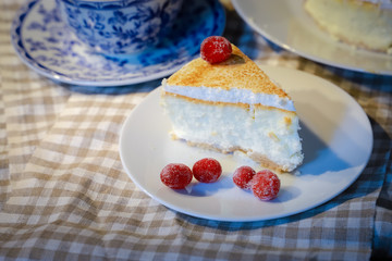 On a dark countertop on a light linen napkin on a white dish, a piece of cheesecake cake decorated with red berries