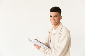 Man holding papers and smiling at camera. Portrait of handsome happy young man writing on paper and looking at camera isolated on grey. Education concept