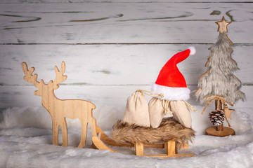 Obraz premium Weihnachtsmütze mit Schlitten, Rentier und Geschenke mit Weihnachtsbaum im Schnee vor einem Holz Hintergrund