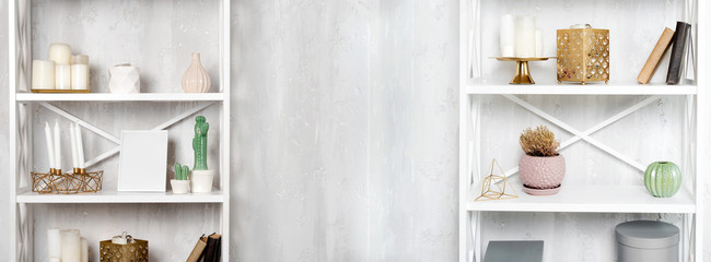 Wooden shelving units with decor near grey wall. Bookcase with photo frame mockup and candles, living room interior details