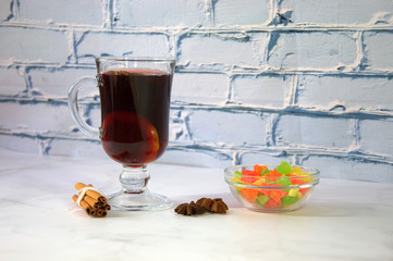 A glass of mulled wine with a slice of orange, anise and a stick of cinnamon is on the table with a...