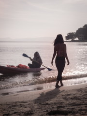 Silhouette of Woman Walking on Sunny Beach with Kayaker Nearby