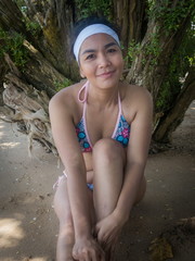 Asian Female with Bikini Sits on Shand in the Shade, Leaning to Camera