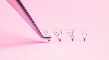 Bunches of fake lashes and tweezers on pink background. Eyelash extension procedure
