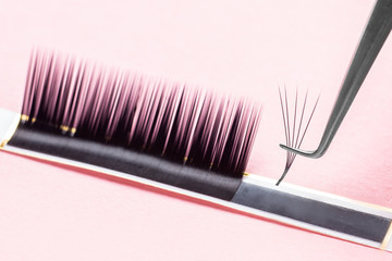 Bunches of fake lashes and tweezers on pink background. Eyelash extension procedure