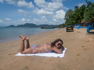 Asian Female with Dark Glasses and Bikini Lies on White Towel on Tropical Beach (Wide View)