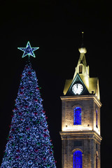 Blue Christmas tree with a blue star next to the chapel and the clock on the tower on the background of the night sky. New Year tree with a chapel on a black background. - obrazy, fototapety, plakaty