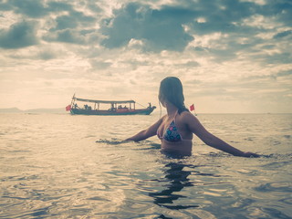 Asian Female Wearing Bikini Moves Arms through the Ocean Waves, with Boat in Background