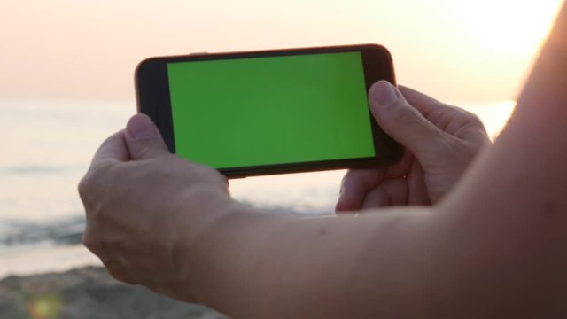 Female holds green screen display phone on the beach 4K video