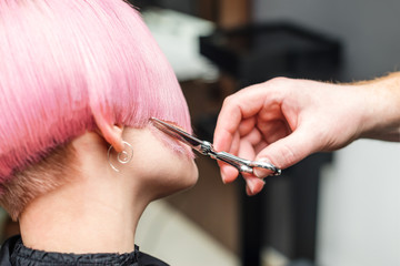 Hand of hair stylist is cuting pink hair close up. Close up oh hsirdresser hand cuts pink hair at beauty salon.