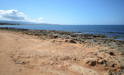 Pink Rocky beach and Mediterranean sea in Sardinia Island. Alghero town in the background