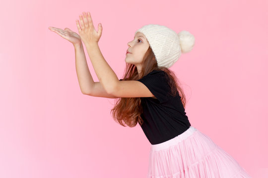 Profile portrait of a cute little girl in white wool hat on pink background, blowing a side part. Space for text.