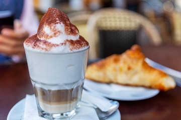 Cappuccino with lush foam and a croissant on a table in a cafe. Close-up.