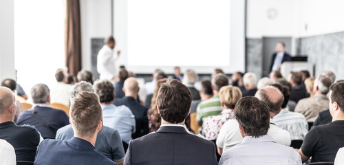 I have a question. Group of business people sitting at the chairs in conference hall. Businessman...
