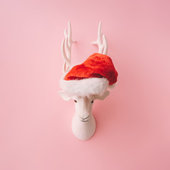 Christmas reindeer decoration with  Santas hat and pink background. Minimal creative concept.