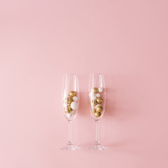 Champagne glasses filled with golden and white glitter decoration and pink background. Celebration minimal Christmas party.