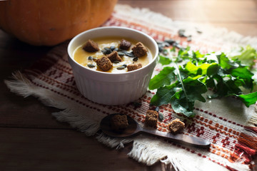 On a wooden table is a cup with soup - mashed potatoes, pumpkin, spoon, pumpkin seeds and arugula.