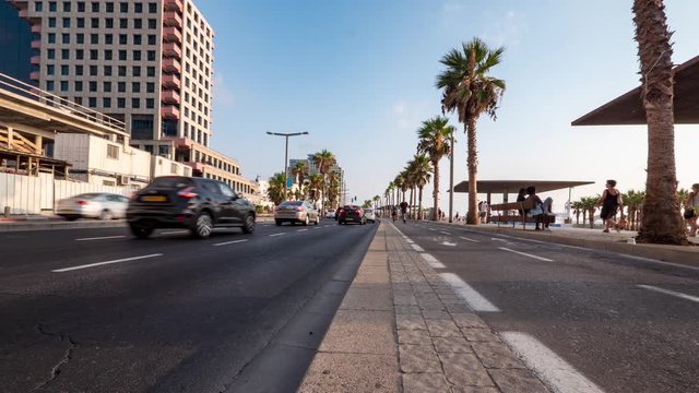 Low angle rising timelapse of a busy street along side a boardwalk in Tel Aviv, Israel with cars, cyclists, and pedestrians on a summer day.