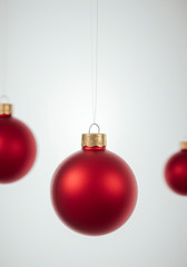 Red Christmas baubles hanging in front of red background.